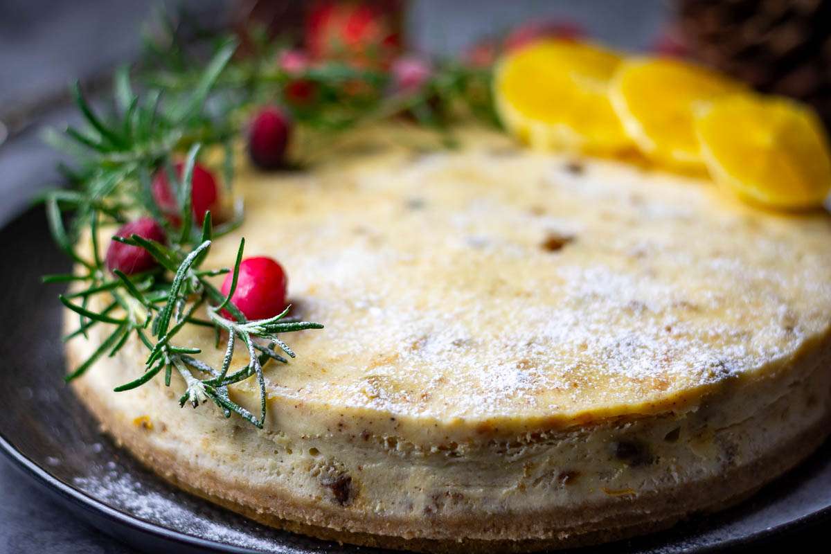 Christmas cake cheesecake decorated with rosemary sprigs, orange spices and cranberries.
