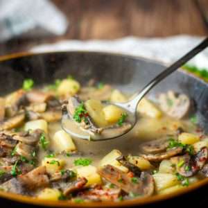 A spoonful of Mushroom and potato soup being lifted out of a bowl of soup.