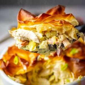A portion of chicken, bacon and leek pie being lifted out of the white pie dish.