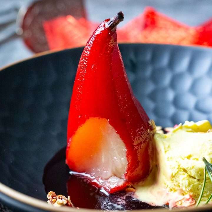 Port poached pear with ice cream in a black bowl.