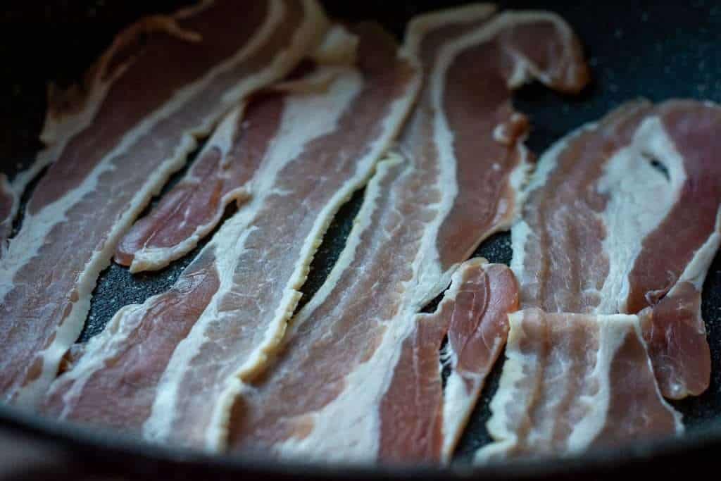 Streaky bacon in a large frying pan.