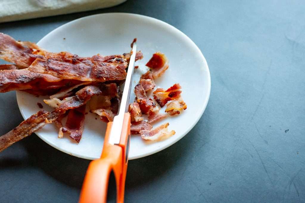 Cutting crispy bacon rashers into small bits with kitchen scissors.