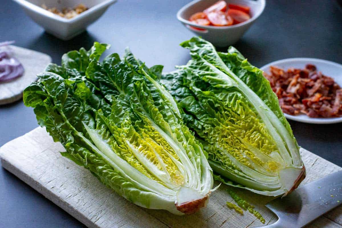 Romaine lettuce cut in half lengthways on a wooden chopping board.