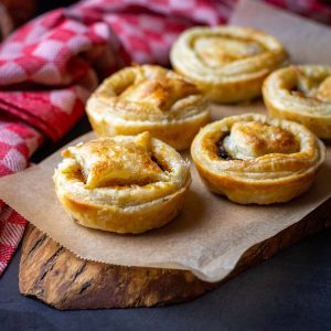 5 puff pastry mince pies arranged on a decorative wooden board.