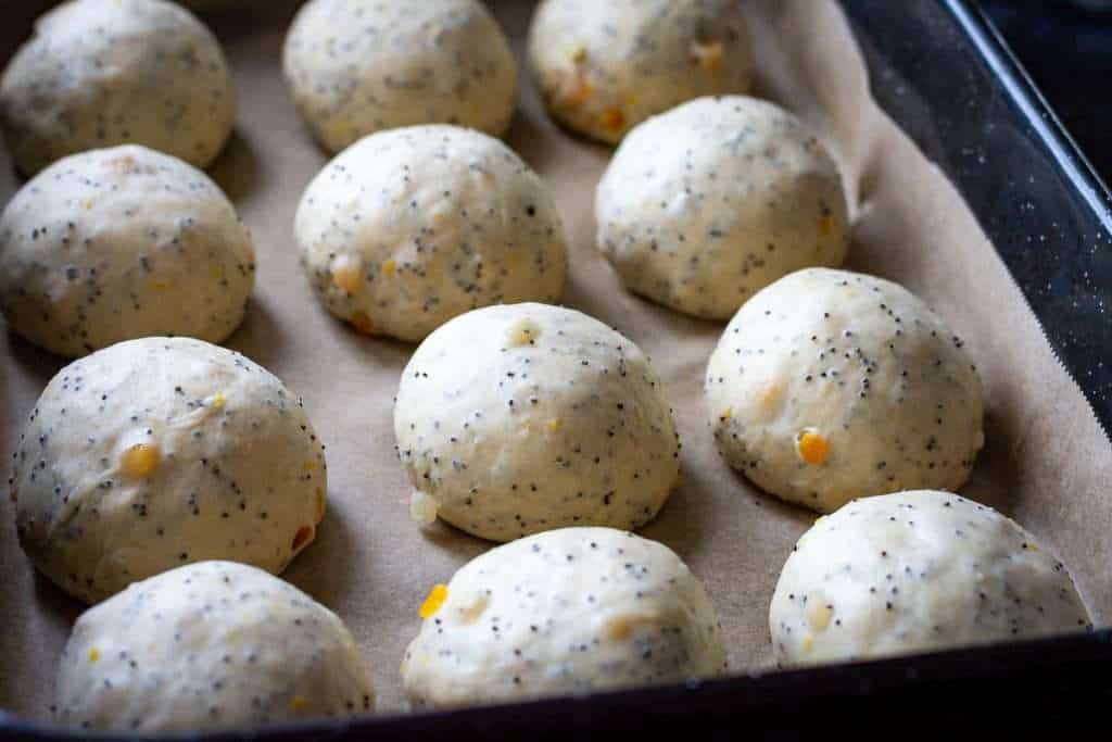 Twelve lemon and poppy seed hot cross buns arranged in a large baking tray.