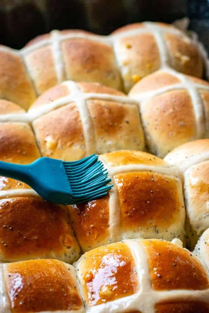 Brushing the freshly baked hot cross buns with lemon glaze using a green pastry brush.