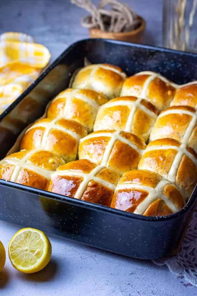 Glazed lemon and poppy seed hot cross buns cooling in a baking tray.