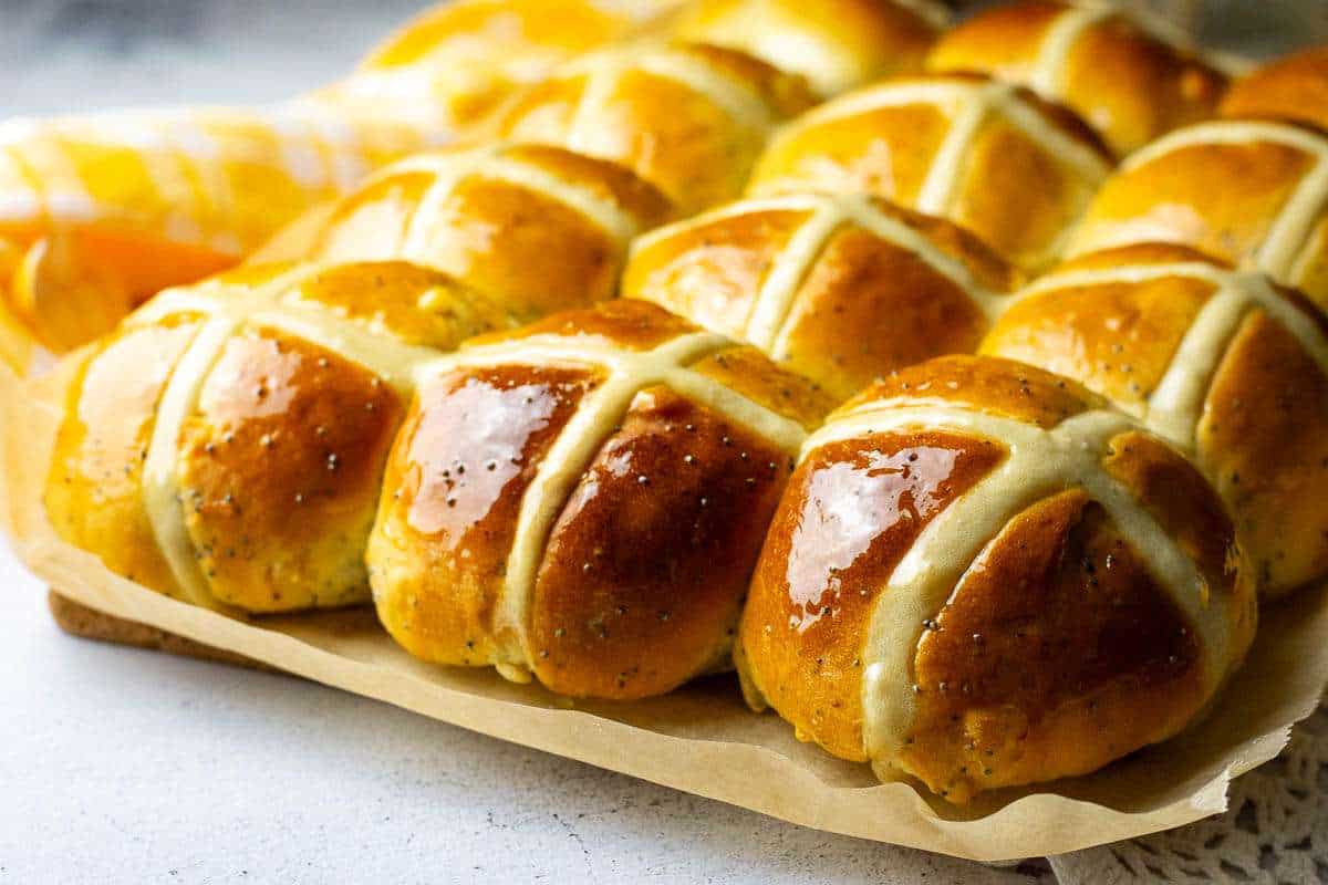 Hot cross buns with lemon and poppy seeds on a piece of parchment paper.