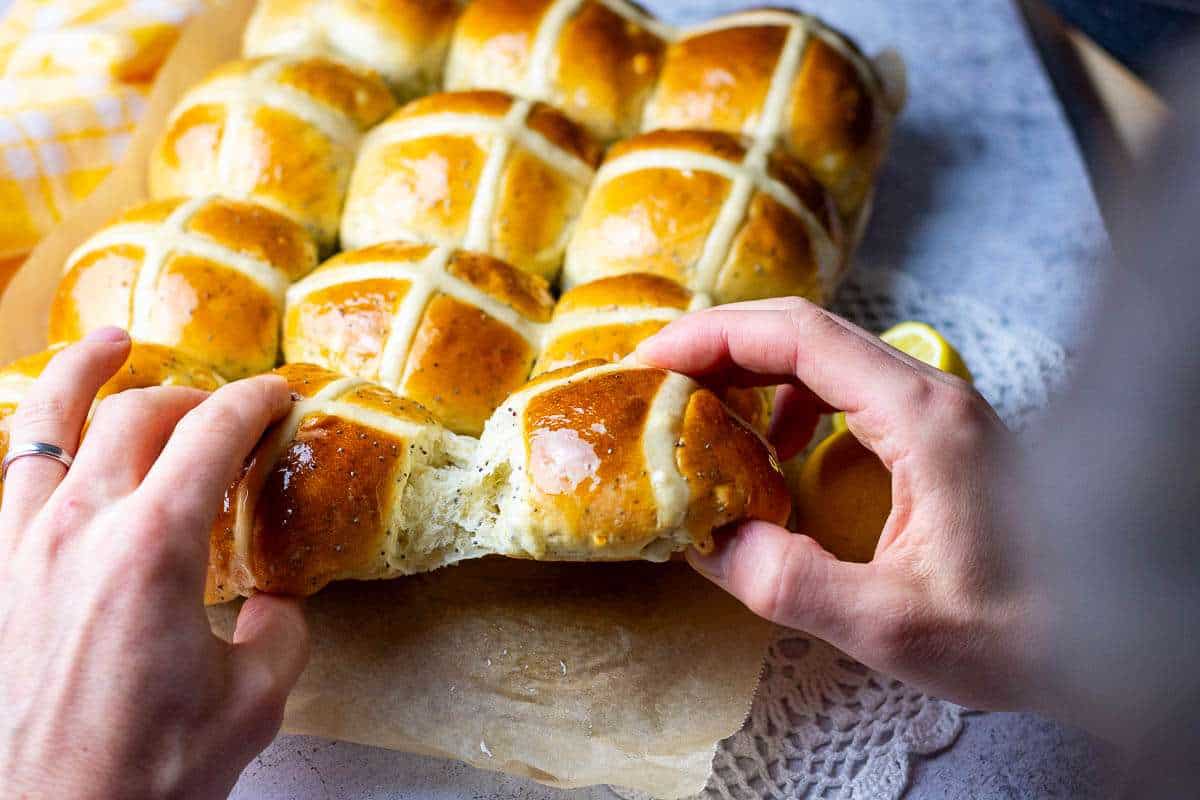 Lemon Poppy Seed Hot Cross Buns being torn apart by two hands.
