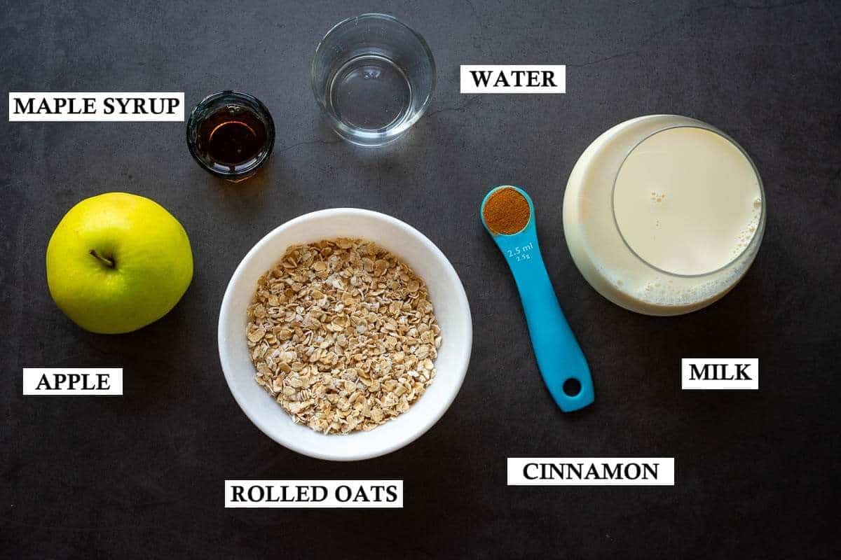 Ingredients for apple porridge with cinnamon on a dark grey surface.