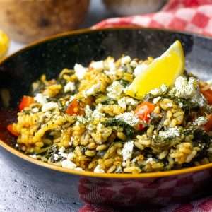Greek spinach rice in a black bowl garnished with a lemon wedge.