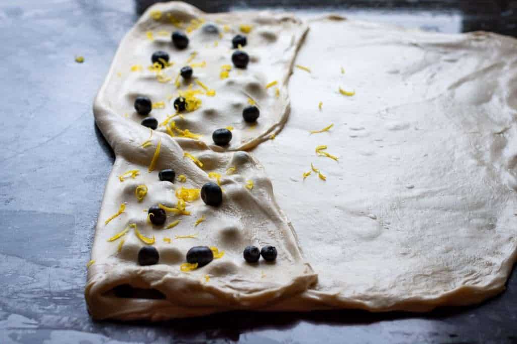 Left side of dough folded over the filling with more blueberries and zest on top.