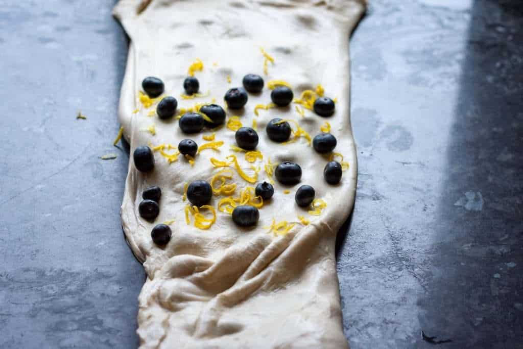 Dough folded like a pamphlet with more blueberries and zest on top.