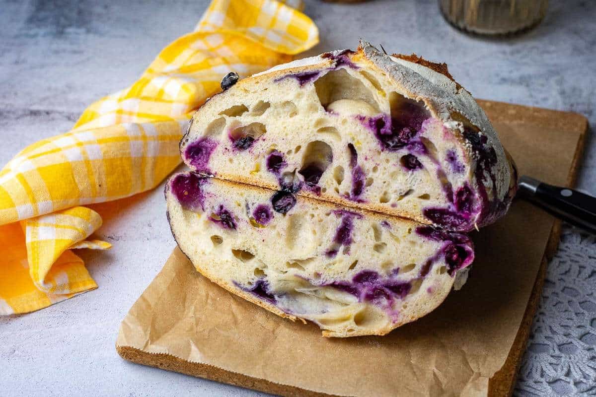 Two halves of sourdough blueberry bread on a wooden cutting board.
