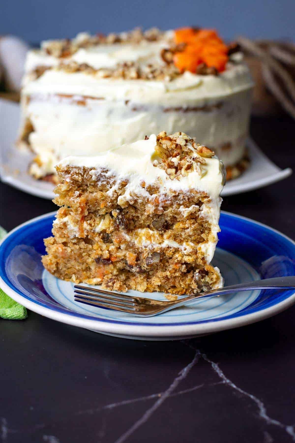 A slice of sourodugh discard carrot cake with cream cheese frosting on a blue plate.