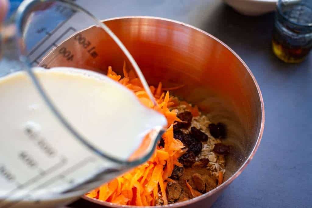 Pouring milk over the other oat porridge ingredients in a small copper pan.
