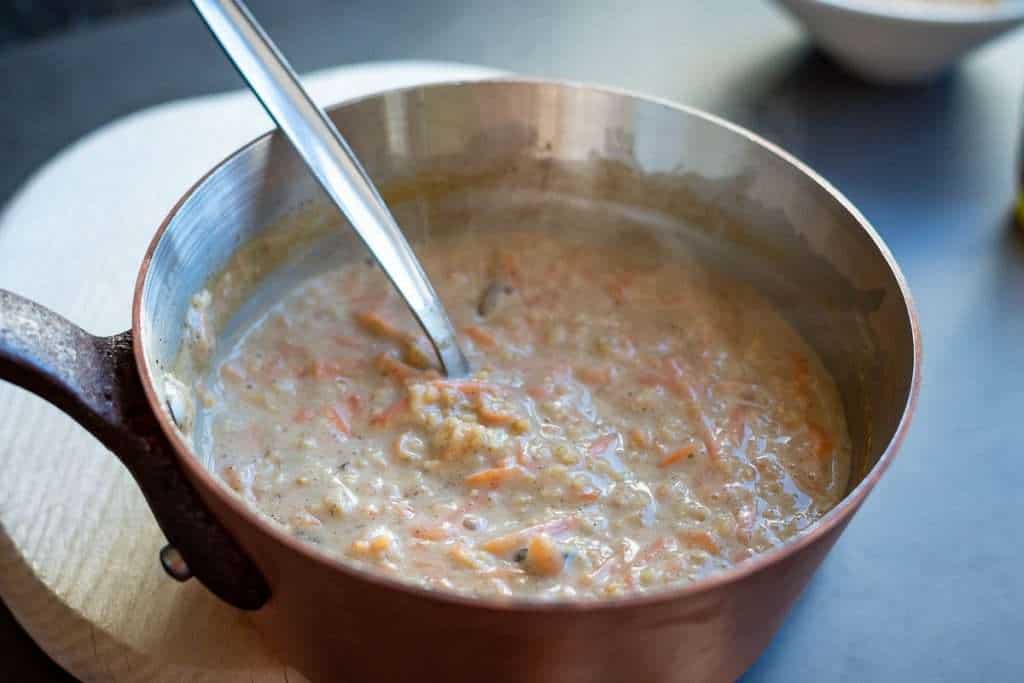 Cooked carrot cake porridge in a pan with a spoon in it.
