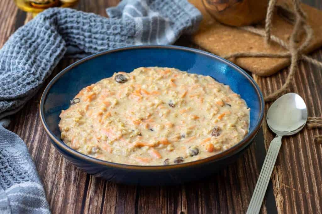 Carrot cake porridge in a blue bowl on a wooden table.