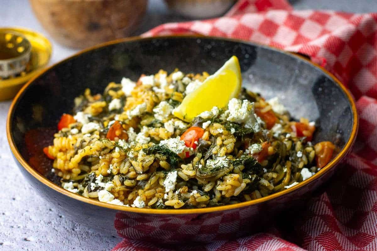 Greek spinach rice in a black bowl garnished with a lemon wedge.