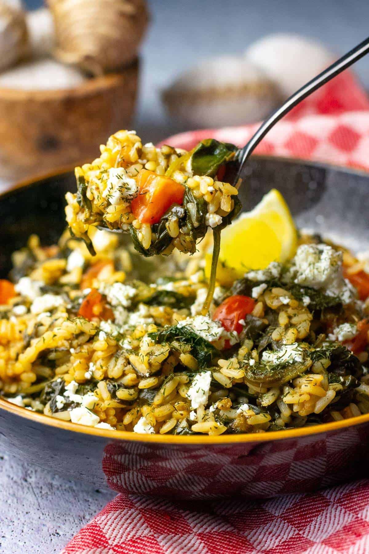 A spoonful of Greek Spinach Rice being picked up from a bowl.