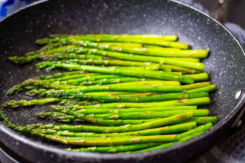 Asparagus frying in butter in a large frying pan.
