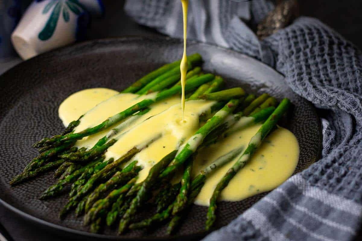 Pouring bearnaise sauce over pan-fried asparagus.
