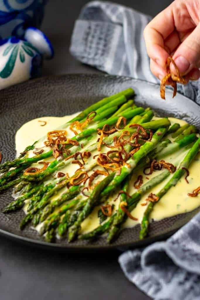 Pan-fried asparagus with homemade bearnaise sauce and crispy fried shallots on a black plate.