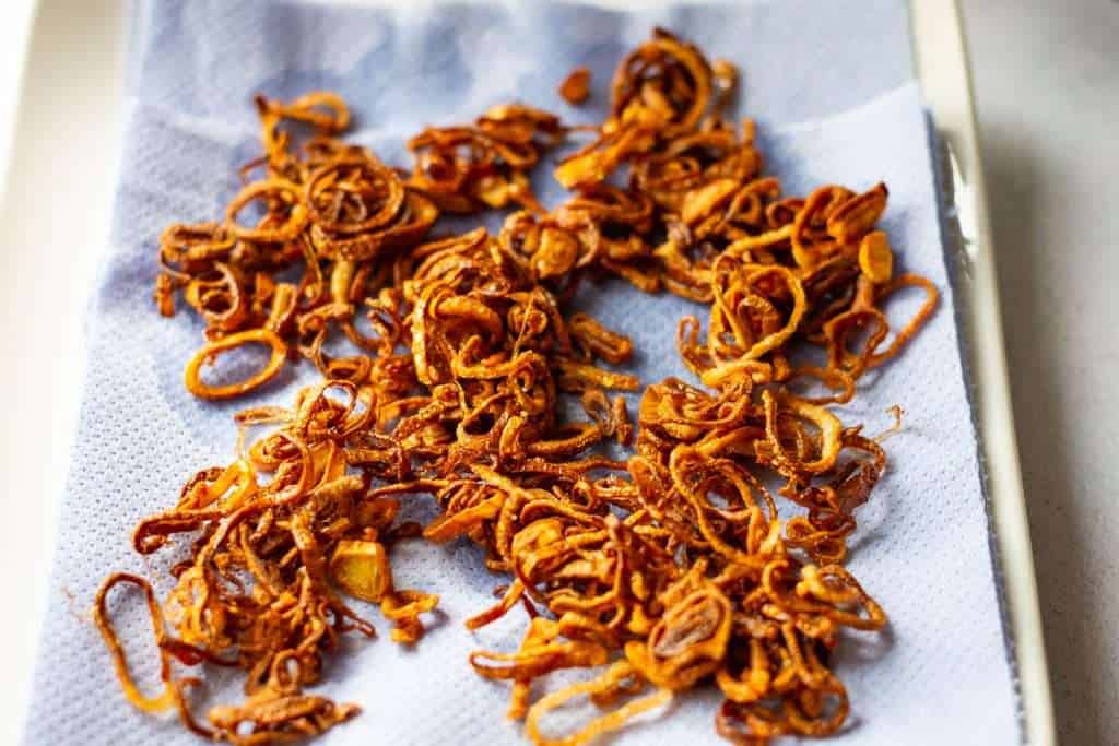 Crispy shallots on a kitchen paper towel lined plate.