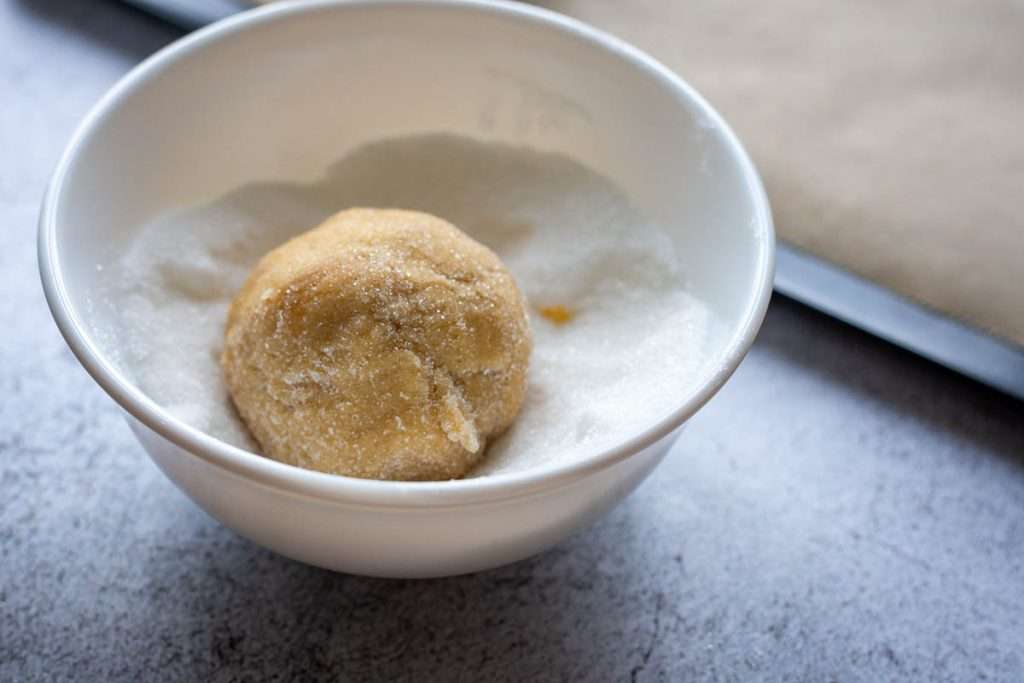 A ball of sourodugh cookie dough in a small bowl of sugar.