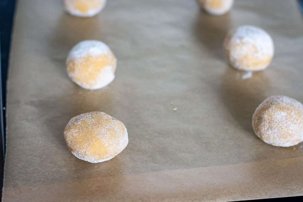 Six sourdough discard peanut butter cookie dough balls on a parchment paper lined baking sheet.