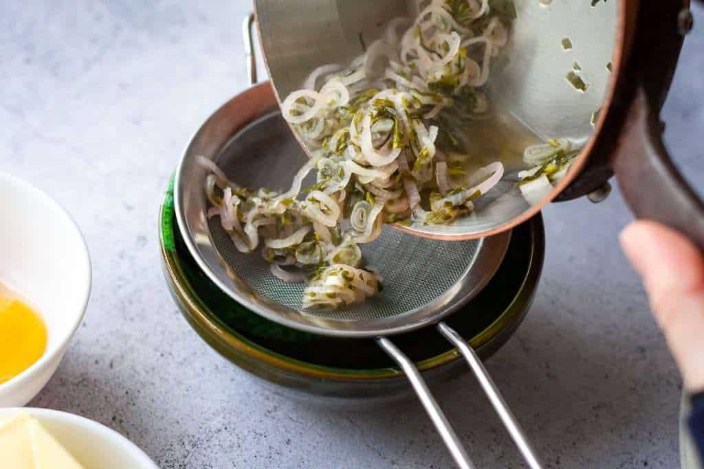 Pouring vinegar deruction through a fine mesh strainer into a bowl.