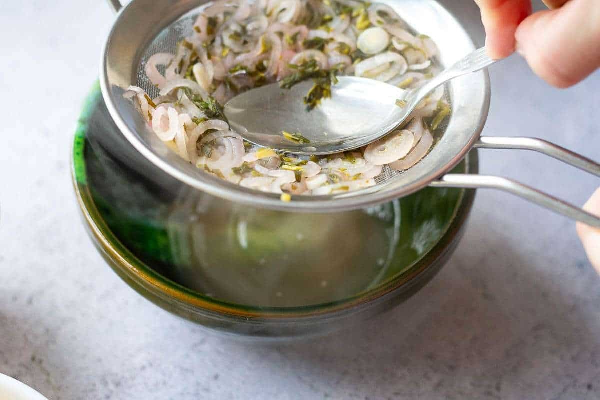 Pressing the shallot and tarragon solids with a spoon to squeeze out the moisture.
