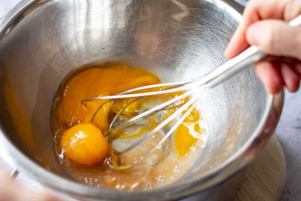 Egg yolks and vinegar reduction in a bain marie about to be whisked with a balloon whisk.