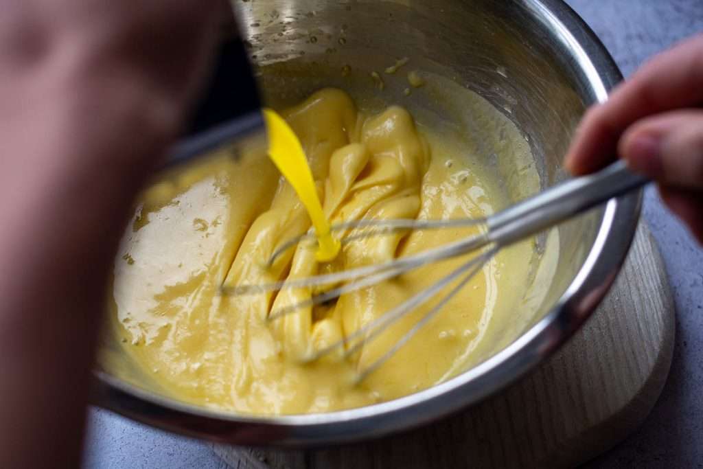 Pouring clarified butter into the egg yolk mixture in a steady stream whilst whisking with ballloon whisk.