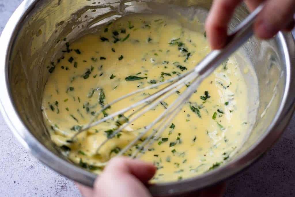 Stirring in fresh tarragon into the prepared bearnaise sauce.