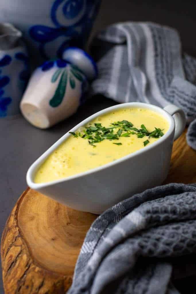 Homemade bearnaise sauce garnished with extra tarragon on a wooden board.