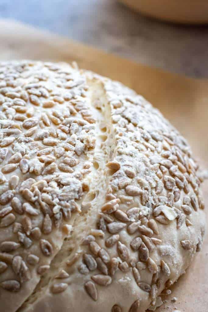 Sourdough With Sunflower Seeds on top with one slash across the side on a piece of parchment paper.