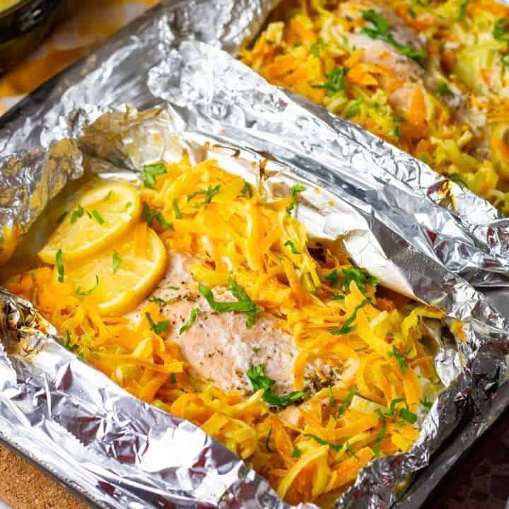 Two unwrapped foil salmon parcels with leeks and carrots.
