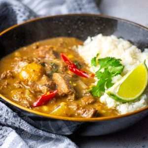 Slow cooker beef massaman curry in a black bowl with rice.