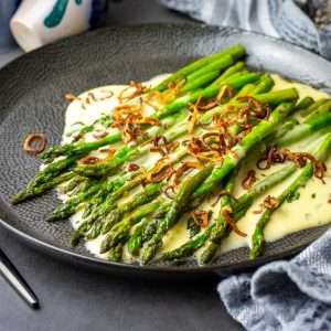 Pan-fried asparagus with homemade bearnaise sauce and crispy fried shallots on a black plate.