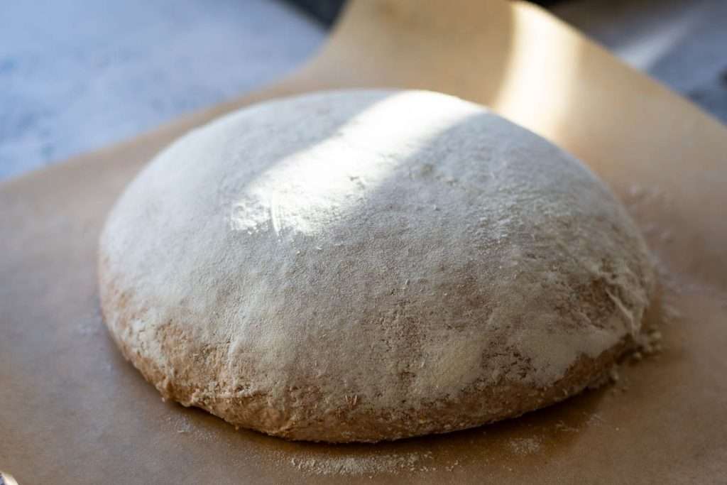 Sourdough ball inverted onto a piece of parchment paper after cold retardation.