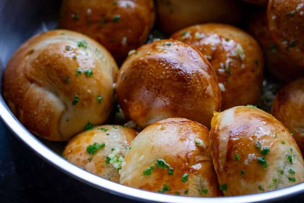 Sourdough knots covered in garlic and parsley butter in a large metal pan.