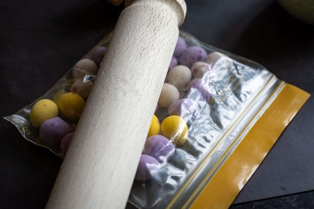 Cadbury mini eggs in a ziplock bag being bashed with a wooden rolling pin.
