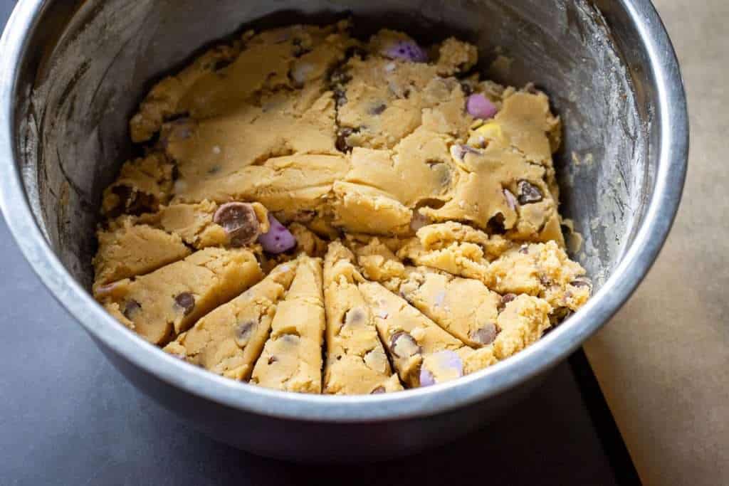 chilled mini egg cookie dough divided into portions within a mixing bowl.