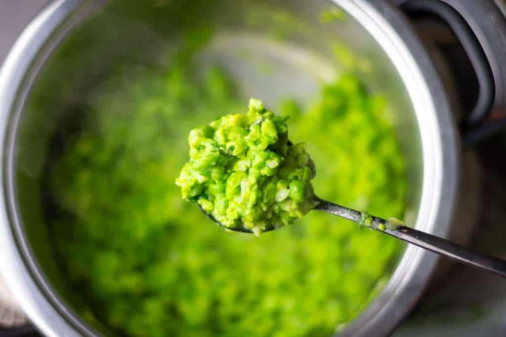 A spoonful of minted mushy peas lifted out of the pan.