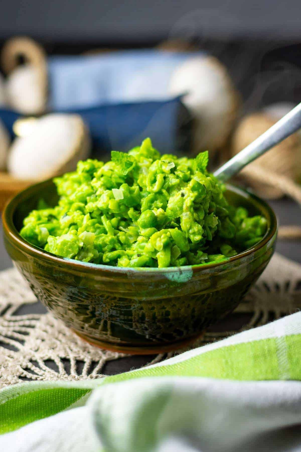 Minted Mushy peas in a dark green bowl with a spoon in it.