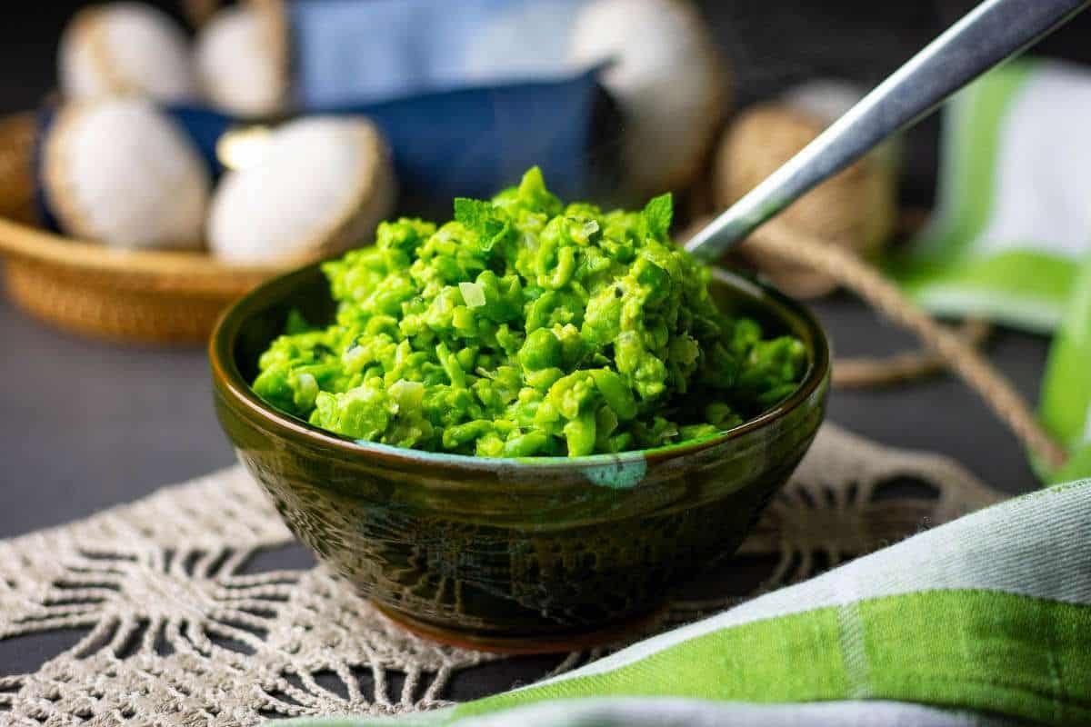 Minted Mushy peas in a dark green bowl with a spoon in it.