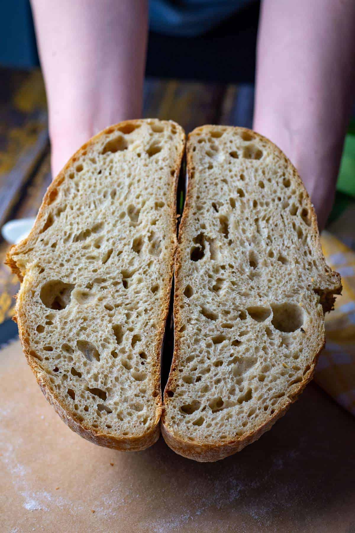 Two halves of Einkorn sourdough bread being hell by two hands.