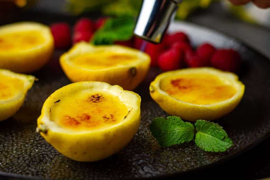 Lemon posset brulee desserts being blow torched to create crunchy caramel topping.