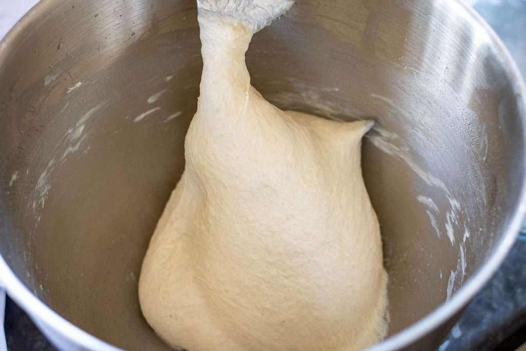 Sourdough focaccia dough gathering around the dough hook in a stand mixer.